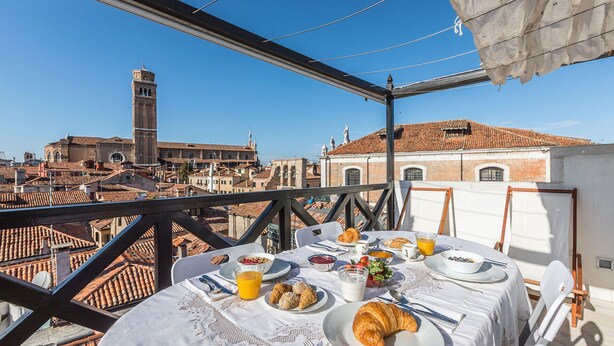 Ein Balkon mit einem Frühstückstisch, Blick auf eine Stadtlandschaft mit historischen Gebäuden und einem markanten Turm.