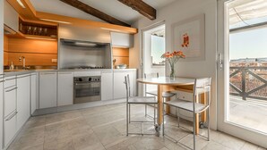 Eine moderne Küche mit weißen Schränken, Edelstahlgeräten und einer Holzbeschichtung. Es gibt eine Essecke mit Tisch und Stühlen, sowie ein Fenster mit Blick auf die Stadt.