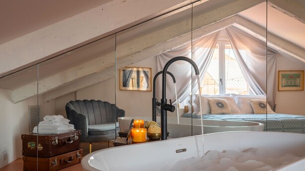 A bedroom with a large white bathtub, a grey sofa, a bed with white bedding, and a window with curtains. - Quiet and Eclectic Apartment next to the Fenice Theatre (Venecia)