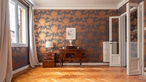 A room with patterned wallpaper, a wooden floor, a desk with a lamp, and a radiator. - Quiet and Eclectic Apartment next to the Fenice Theatre (Venecia)