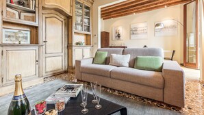 Een woonkamer met een bank, een bijzettafeltje met tijdschriften en glazen, een kast met decoratieve objecten, en een houten plafond.