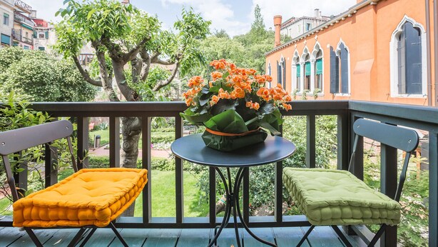 Een balkon met twee comfortabele stoelen en een tafel, een bloempot met oranje bloemen, en een uitzicht op een gebouw met gebogen ramen.