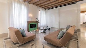 A modern living room with two sofas, a glass coffee table, a fireplace, and a large window with curtains. - Minimalist Bright and Spacious Designer Home (Venecia)