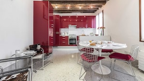 A modern kitchen with red cabinets, a white countertop, and a dining area with a round table and red chairs. - Minimalist Bright and Spacious Designer Home (Venecia)