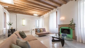 A spacious living room with a wooden ceiling, a green fireplace, a glass coffee table, and a beige sofa with patterned cushions. - Minimalist Bright and Spacious Designer Home (Venecia)