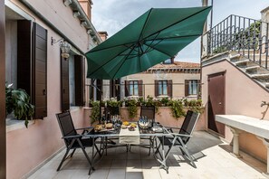 An outdoor patio with a table set for dining, surrounded by a green umbrella, and a staircase leading to an upper level. - Elegant 6-bedroom penthouse with a terrace and a view of the canal (Venecia)