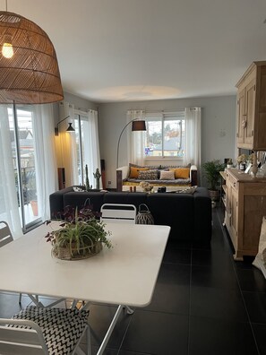 A modern living room with a sofa, a dining table with chairs, and a kitchen area with cabinets.