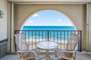 A balcony with two wicker chairs and a small round table, overlooking a beach with the ocean and a clear sky. - Gorgeous 2 Bedroom condo with outdoor pool and ocean views! (Ocean City)
