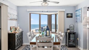 Ein Esszimmer mit Blick auf den Strand, einem Deckenventilator und einem großen Fenster.