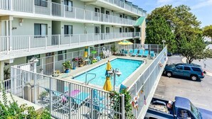 A multi-story hotel with a rooftop pool area, outdoor seating, and a parking lot.