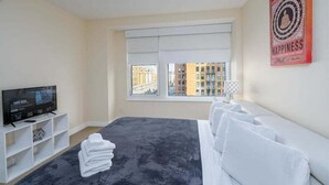 Una habitación de hotel con cama, televisión, ventana con vista a la ciudad y un cartel en la pared.