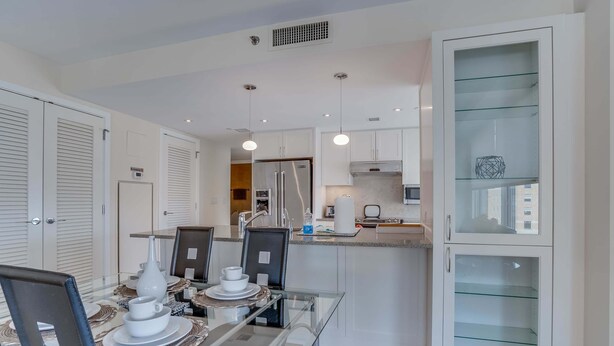 A modern kitchen with a glass dining table, white cabinetry, and a built-in display cabinet.