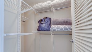 A storage closet with white metal shelving, a purple bag, and patterned bedding.