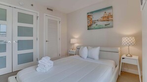 A hotel room with a bed, two bedside tables with lamps, a painting of a cityscape, and a door with frosted glass panels.
