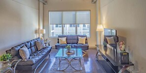Una sala de estar con sofá, mesa de centro, televisor y un amplio ventanal.