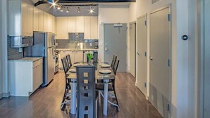 A modern kitchen with stainless steel appliances, a dining area with a glass table, and a hallway with doors. - Midtown Fully Furnished Apartments - Great Location 2 Bedroom Apts by RedAwning (Atlanta)