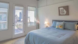 A bedroom with a bed, two windows, a door, and a wall-mounted sign. - Midtown Fully Furnished Apartments - Great Location 2 Bedroom Apts by RedAwning (Atlanta)