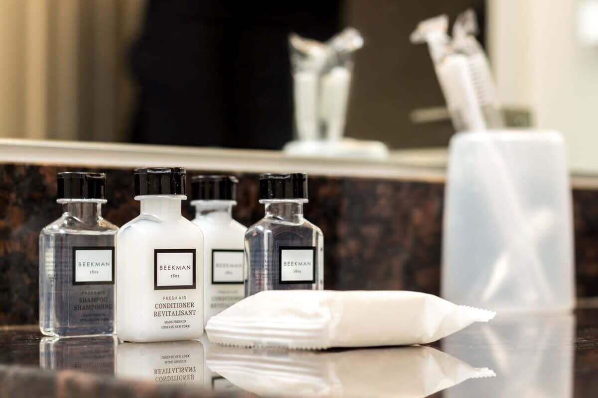 A bathroom counter with three bottles of Beekman Fresh Air Conditioner Revitalisant, a white towel, and a toothbrush holder with toothbrushes.
