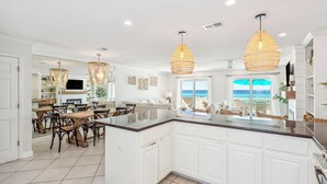 Una cocina amplia con armarios blancos, una isla grande e iluminación colgante.