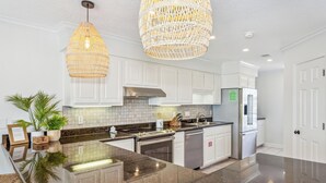 Una cocina moderna con armarios blancos, encimera de granito, electrodomésticos de acero inoxidable y dos lámparas colgantes de mimbre.