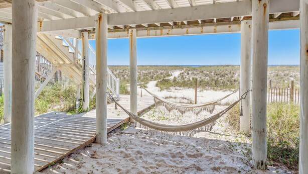 Una estructura frente a la playa con una hamaca, muelle de madera y vistas a la playa y las dunas.