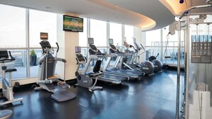 A gym with treadmills, ellipticals, and exercise balls, large windows, and a view of the city.