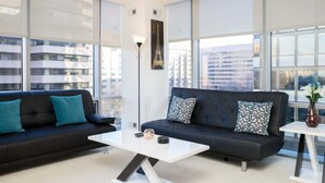 A modern living room with two dark sofas, a white coffee table, and large windows offering city views.