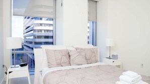 A modern hotel room with a large bed, two bedside tables, and a view of a high-rise building.