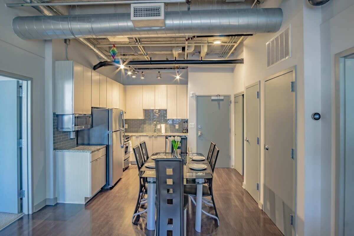 A modern kitchen with stainless steel appliances, a dining area with a table and chairs, and a hallway with doors.
