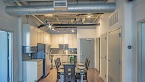 A modern kitchen with stainless steel appliances, a dining area with a table and chairs, and a hallway with doors.