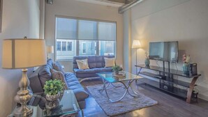 A modern living room with a sofa, coffee table, TV stand, and large windows.