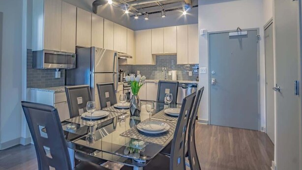 A modern kitchen with stainless steel appliances, a dining table set for four, and a door on the right.