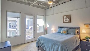A bedroom with a bed, a nightstand, a lamp, a ceiling fan, and a view of the outside.