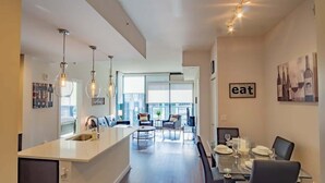 Eine moderne Küche mit Kochinsel, Essbereich mit Glastisch und Wohnbereich mit Sofa und Sesseln.