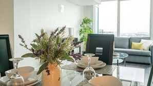 A modern living room with a dining table set for four, a sofa, a coffee table, and a large window offering a view. - 2br Furnished Apartment In Baltimore Downtown 2 Bedroom Apts by RedAwning (Baltimore)