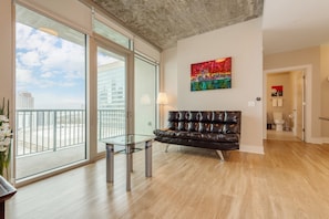 Relax in a stylish living area with a large sliding door opening to a city view, a black leather sofa, and a vibrant abstract painting.