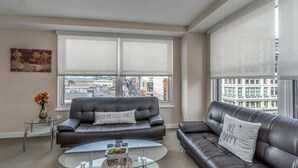 Ein modernes Wohnzimmer mit zwei schwarzen Ledersofas, einem Glastisch und einem großen Fenster mit Jalousien.