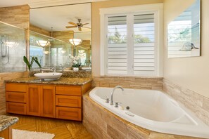 Ein Badezimmer mit einer großen Badewanne, Holzschränken, einem Waschtisch und einem Deckenventilator.