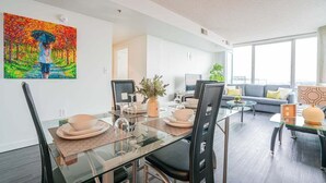 A modern living room with a glass dining table, black chairs, a sofa, and a large window.
