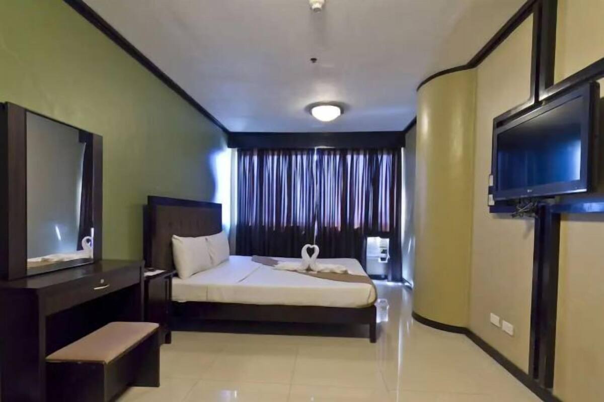Quarto de hotel com cama, um banco, uma TV e uma cortina.
