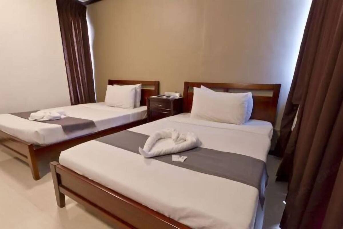 Duas camas de solteiro com estrutura de madeira, lençóis brancos e uma toalha dobrada em cada cama.