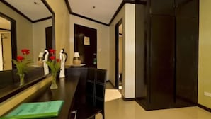 A hotel lobby with a long reception desk, a black chair, and a mirror reflecting the room. There are vases with red flowers on the desk.