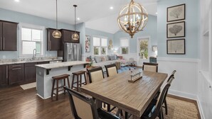 A spacious kitchen with dark cabinets, a central island with stools, and pendant lighting. - Close to Dining & Shopping, 1-Floor Cottage, Pool + Free Attraction Tickets! (Santa Rosa Beach)