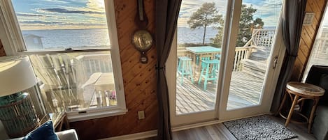 Une pièce chaleureuse avec un plancher en bois, une vue sur une terrasse aménagée avec du mobilier d’extérieur et une grande fenêtre avec des rideaux.