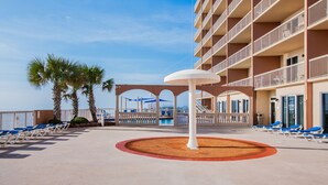 Zona de piscina en un resort con sillones de descanso, palmeras y un edificio con balcones.