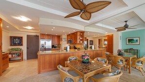 Una cocina amplia con armarios de madera, una isla central y una zona de comedor con sillas de mimbre.