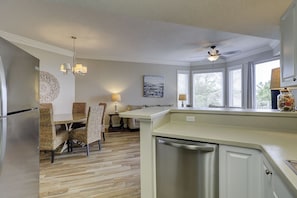 A kitchen with a dishwasher, a dining area with chairs, a ceiling fan, and a window with blinds.
