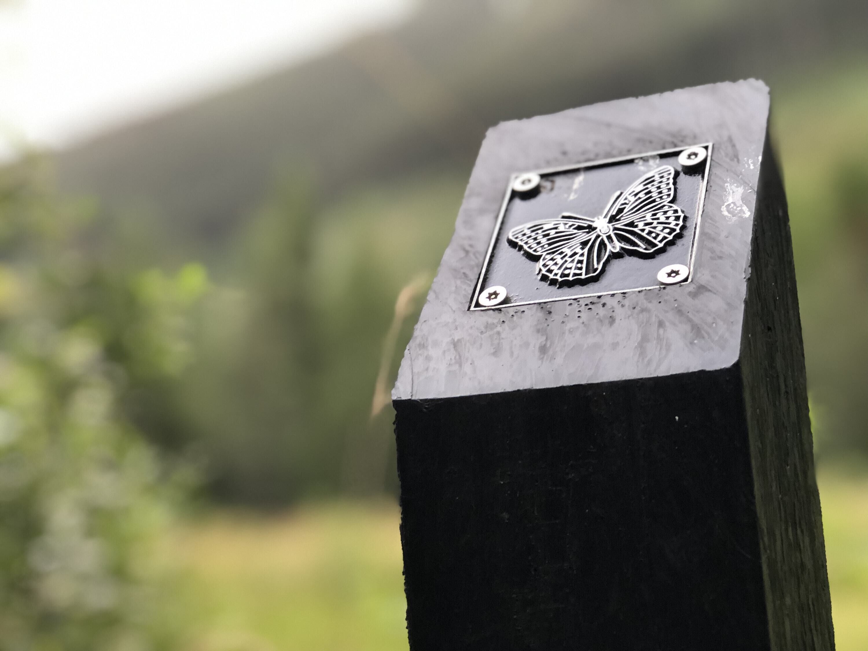 A metal plaque with a butterfly design on a wooden post.