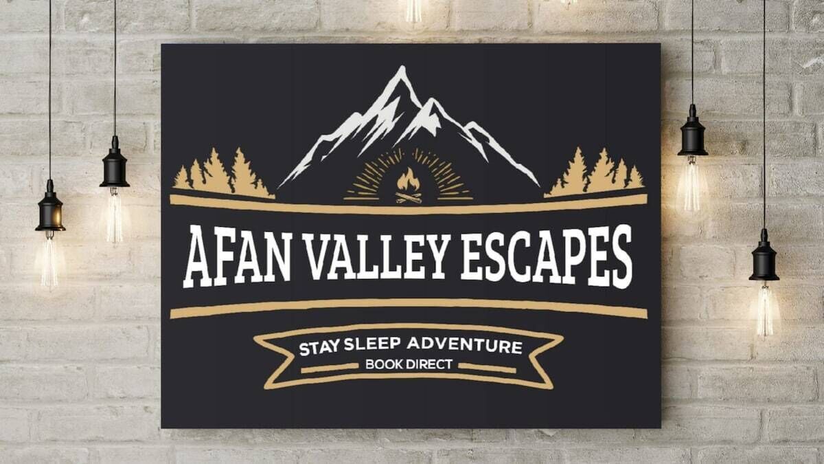 A wall-mounted sign with a mountain and forest graphic, text reading "AFAN VALLEY ESCAPES," and a tagline "STAY SLEEP ADVENTURE BOOK DIRECT."