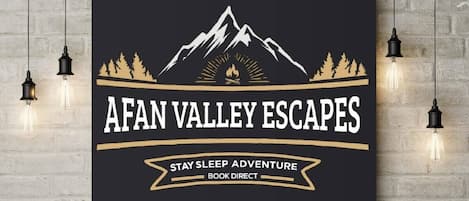 A wall-mounted sign with a mountain and forest graphic, text reading "AFAN VALLEY ESCAPES," and a tagline "STAY SLEEP ADVENTURE BOOK DIRECT."
